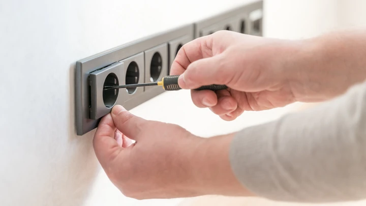 Manos manipulando un enchufe en una toma eléctrica, representando riesgos de descarga y seguridad en dispositivos eléctricos.