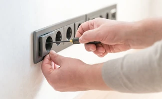 Manos manipulando un enchufe en una toma eléctrica, representando riesgos de descarga y seguridad en dispositivos eléctricos.
