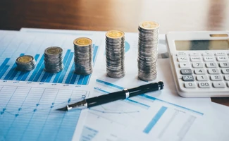 Monedas, calculadora y documentos financieros sobre una mesa, representando la preparación de documentación para solicitar financiación empresarial.