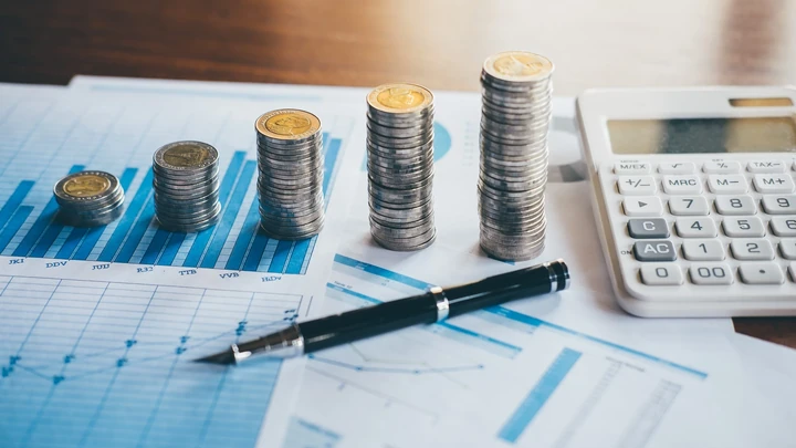 Monedas, calculadora y documentos financieros sobre una mesa, representando la preparación de documentación para solicitar financiación empresarial.